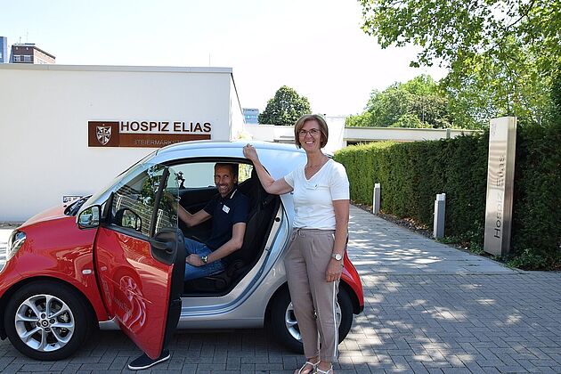 Frau und Mann im Elektroflitzer vor dem Hospiz Elias